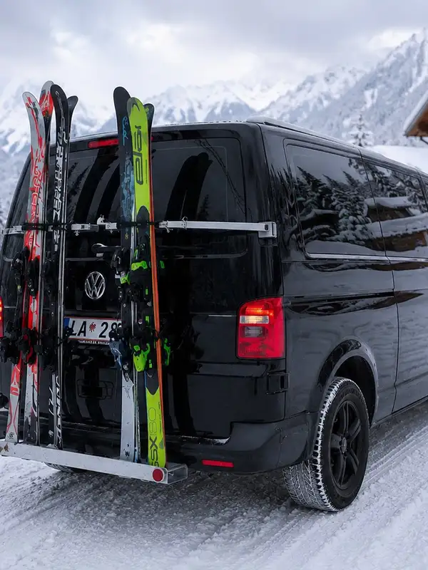 Alpinum Taxi VW Caravelle 4x4 with skis on the rear rack on a snow-covered road on the Arlberg